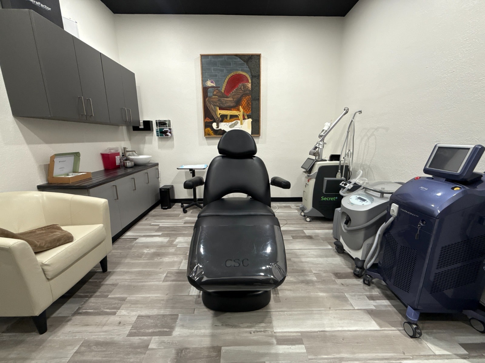 Harmony Med Spa laser treatment room with a black reclining chair, gray cabinets, and treatment devices